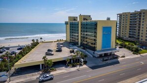 Un hôtel doté d’un parking, offrant une vue sur la plage et comprenant un grand bâtiment avec une porte bleue.