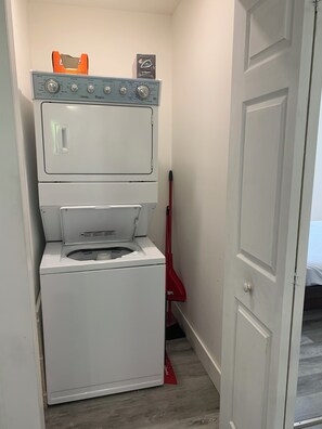 Ein kleiner Hauswirtschaftsraum mit einer Waschmaschine und einem Trockner, einem Mop und einer Tür zu einem anderen Raum.