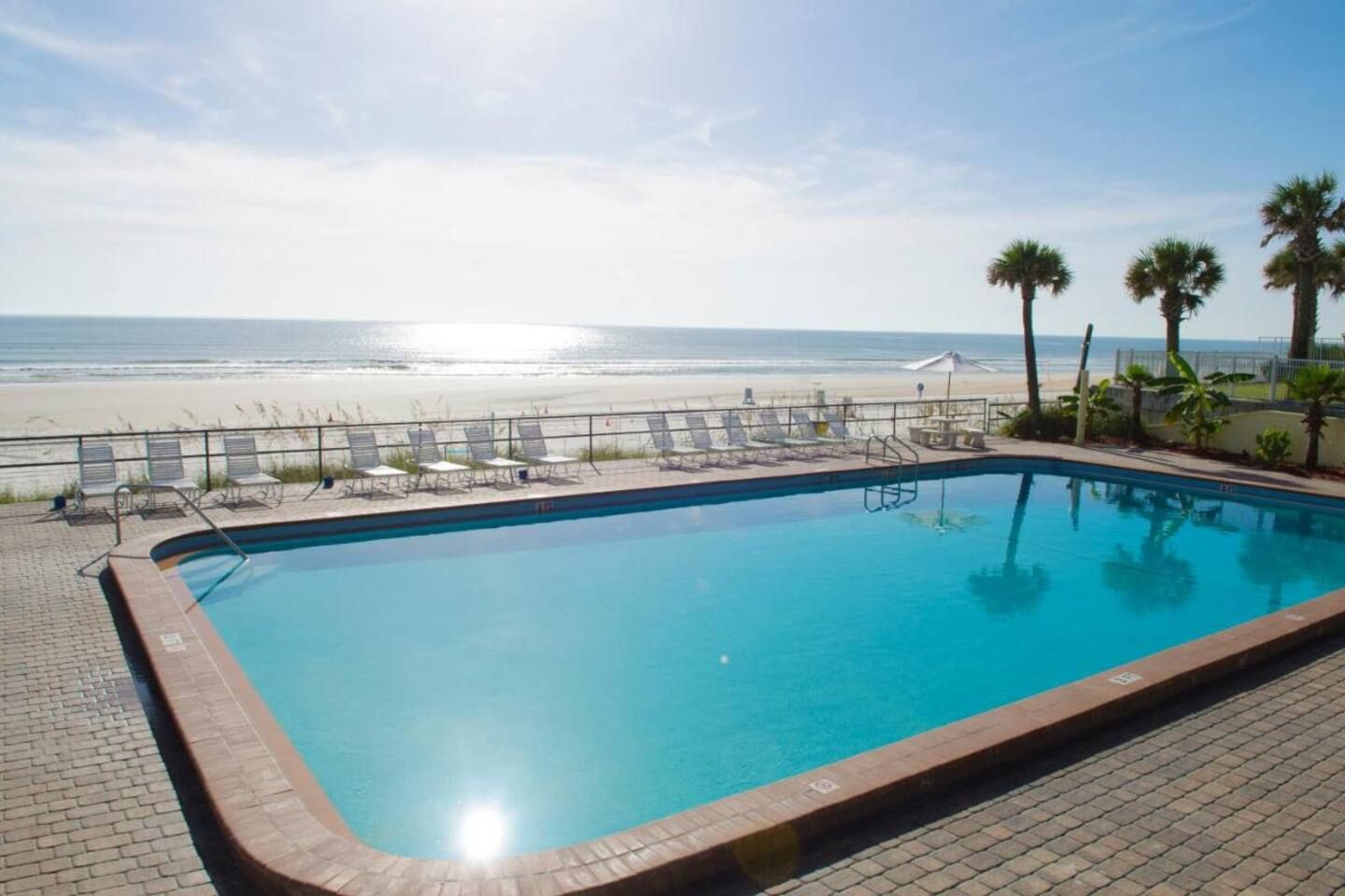 A swimming pool with a view of the beach and palm trees.