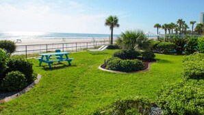Área gramada com mesa para piquenique e vista para a praia.