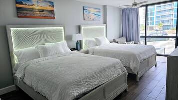 Habitación de hotel con dos camas, ventilador de techo y ventanas grandes con vista a la ciudad.