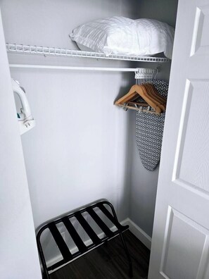 A narrow room with a white door, a metal drying rack, a white shelf with a pillow, and a patterned ironing board. - Newly renovated 2 queen studio w/kitchenette, pool (Daytona Beach)