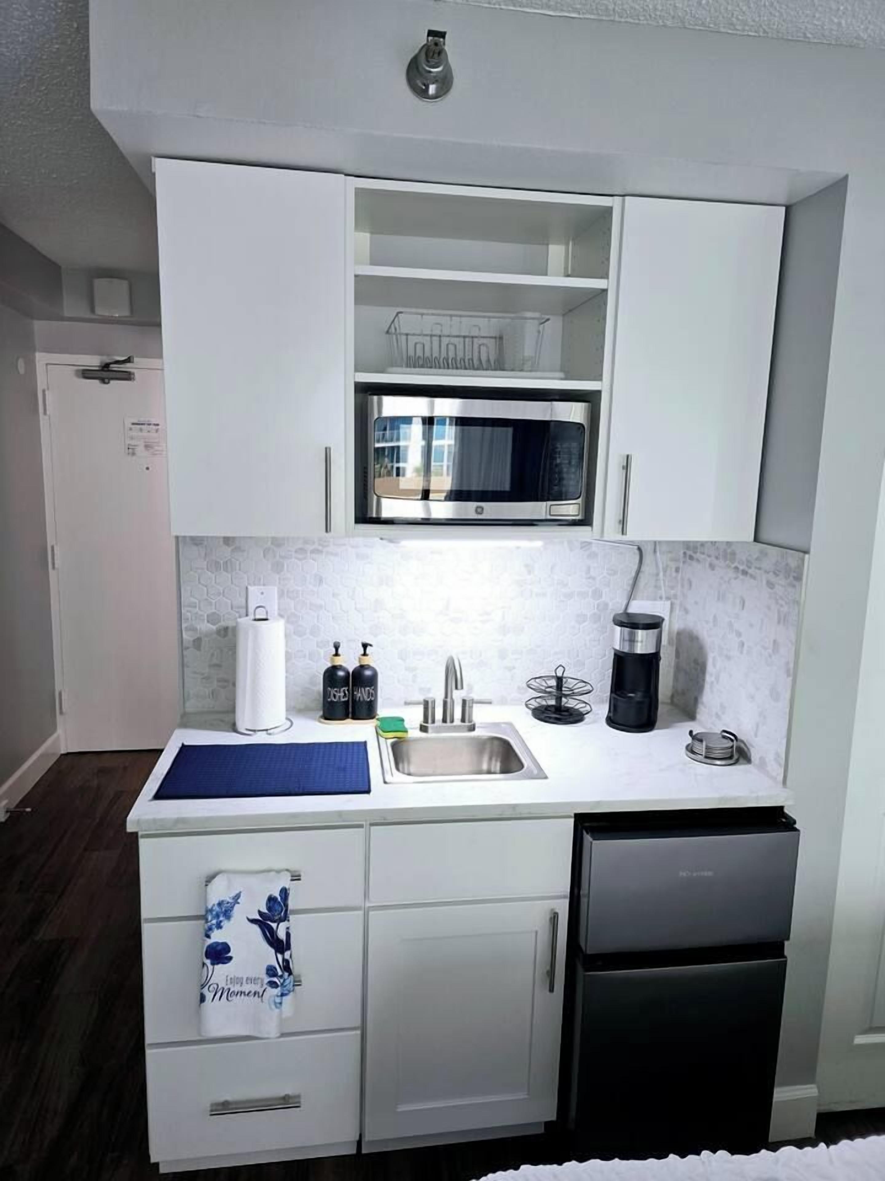 A compact kitchen with white cabinetry, a microwave, a sink, and a dishwasher.