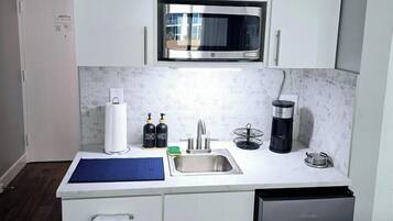 A compact kitchen with white cabinetry, a microwave, a sink, and a dishwasher.