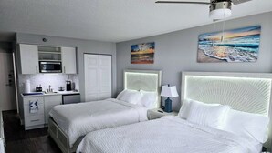 Quarto de hotel com duas camas, uma cozinha compacta e obras de arte nas paredes.