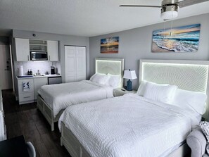 Habitación de hotel con dos camas, kitchenette y obras de arte en las paredes.