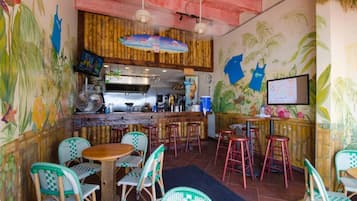 A restaurant interior with a bar area, high stools, and a mural of tropical plants.