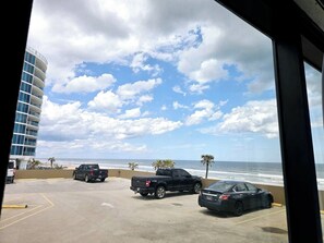 A parking area with vehicles, a view of the ocean, and a building with a curved facade. - Newly renovated 2 queen studio w/kitchenette, pool (Daytona Beach)