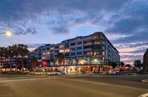Un hôtel à plusieurs étages, doté d’une architecture moderne, situé à l’angle d’une rue, à un carrefour bien visible.