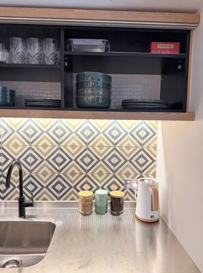 A kitchen with a stainless steel sink, a patterned backsplash, and storage shelves with kitchenware. - Luxury Studio Bondi Beach Front (Bondi Beach)