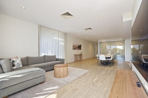 A modern living room with a grey sofa, a round wooden coffee table, and a dining area with a white table and chairs. - Starboard Cove (Safety Beach)
