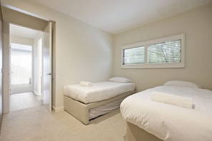A bedroom with two beds, a window with blinds, and a door leading to another room. - Starboard Cove (Safety Beach)