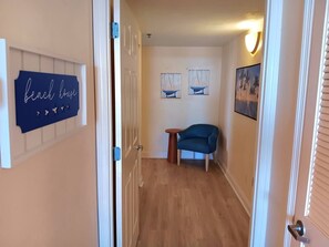 A hallway with a wooden floor, a blue chair, and wall decorations including a 'beach house' sign and two framed pictures. - Spacious 1bdrm direct oceanfront w/private balcony (Daytona Beach)
