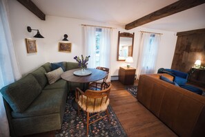 A cozy living room with a green sofa, a wooden coffee table, a blue armchair, and a patterned rug. - Garden Gate Farmhouse- a peaceful retreat with hot tub and hammocks! (Skaneateles)