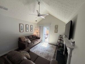 A living room with a brown leather sofa, a ceiling fan, a fireplace, and a television mounted on the wall. - ATL Hideaway....2-bedroom house in tranquil Atlanta perfect for a relaxing stay (Atlanta)
