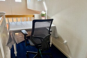 A room with a bed, a desk with a chair, a power outlet, and a white wall.