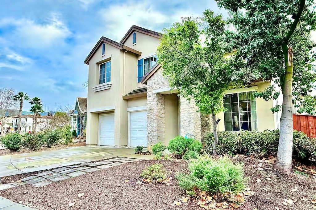 A two-story house with a garage, a stone facade, and a well-maintained front yard with shrubs and a tree.