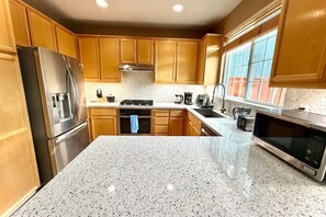 Una cocina con armarios de madera, electrodomésticos de acero inoxidable, encimeras de granito y un ventanal que proporciona luz natural.