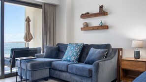 A modern living room with a grey sectional sofa, a small table, and a lamp. There are wooden shelves with decorative items on the wall. - One 503B Studio: Vista del Sol Studio (Puerto Peñasco)