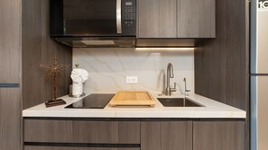 Een moderne keuken met een ingebouwde magnetron, een houten snijplank en een gootsteen met een kraan.