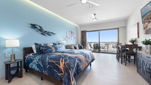 A modern bedroom with a large bed, a desk, and a balcony with a city view. - Two 1107A Studio : Ocean Waves Retreat (Puerto Peñasco)