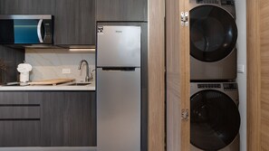 Eine kompakte Küche mit Mikrowelle, Kühlschrank, Spüle und zwei übereinander angeordneten Waschmaschinen.