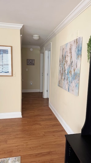 A hallway with wooden flooring, a painting on the wall, and a door with a sign.