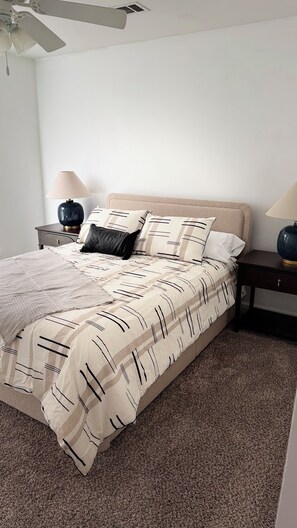 A bedroom with a bed, two nightstands, a ceiling fan, and a carpeted floor.