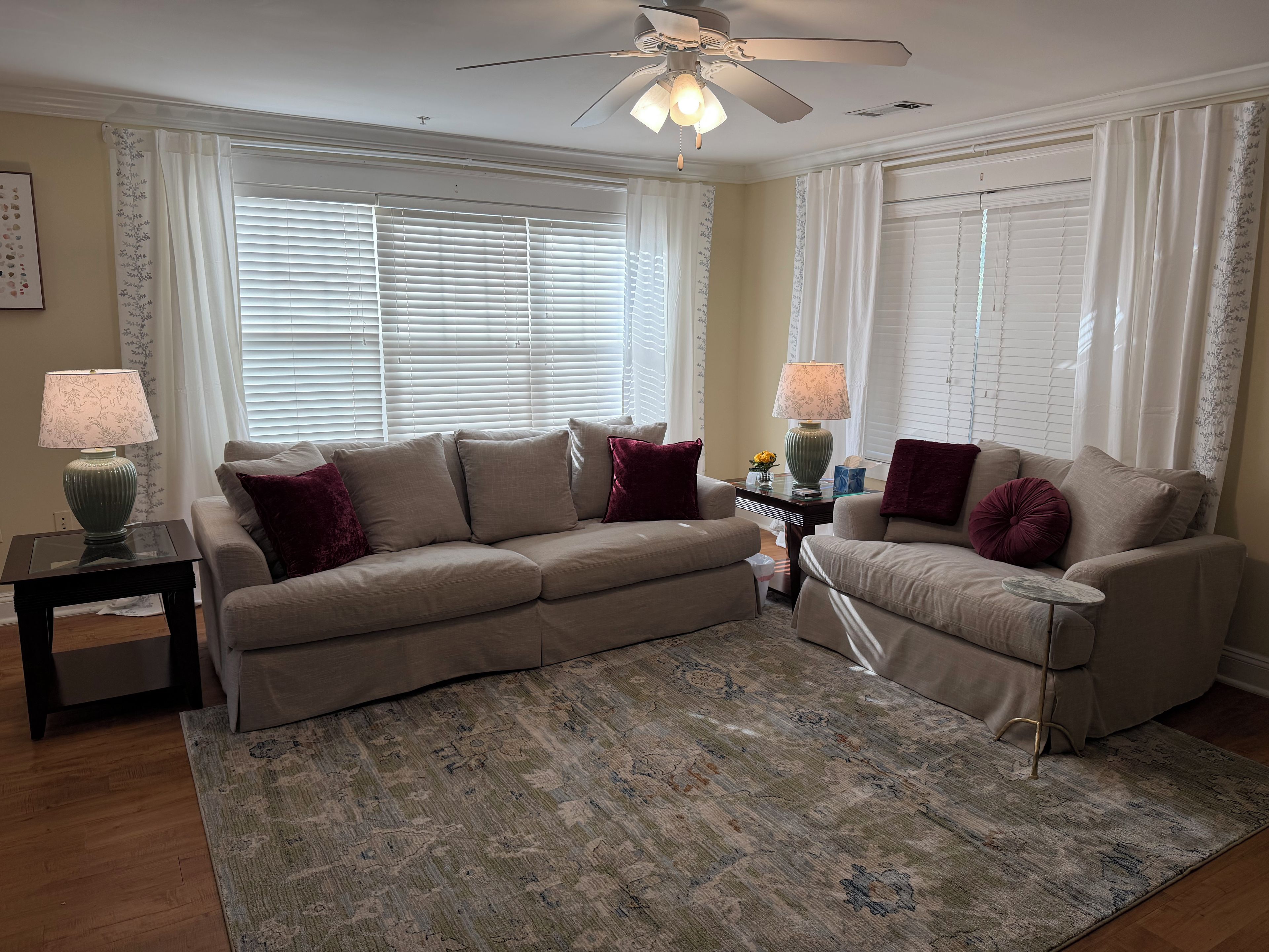 A living room with a beige sofa, two side tables with lamps, a patterned rug, and a ceiling fan.
