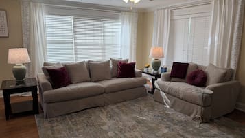 A living room with a beige sofa, two side tables with lamps, a patterned rug, and a ceiling fan.