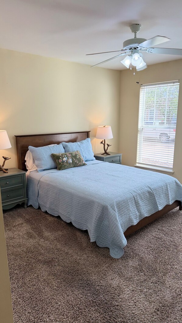 A bedroom with a bed, two bedside tables, a ceiling fan, and a window with blinds.