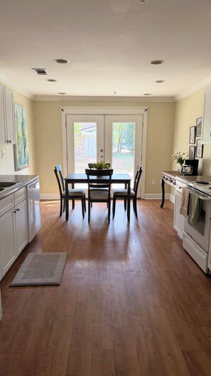 A spacious kitchen with a dining area, wooden floors, and a view through the glass doors.