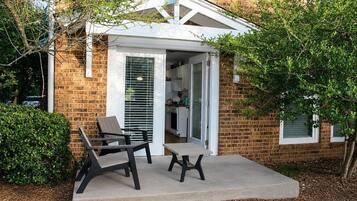 A brick house with a covered patio, a dining area with chairs, and a kitchen visible through an open door.