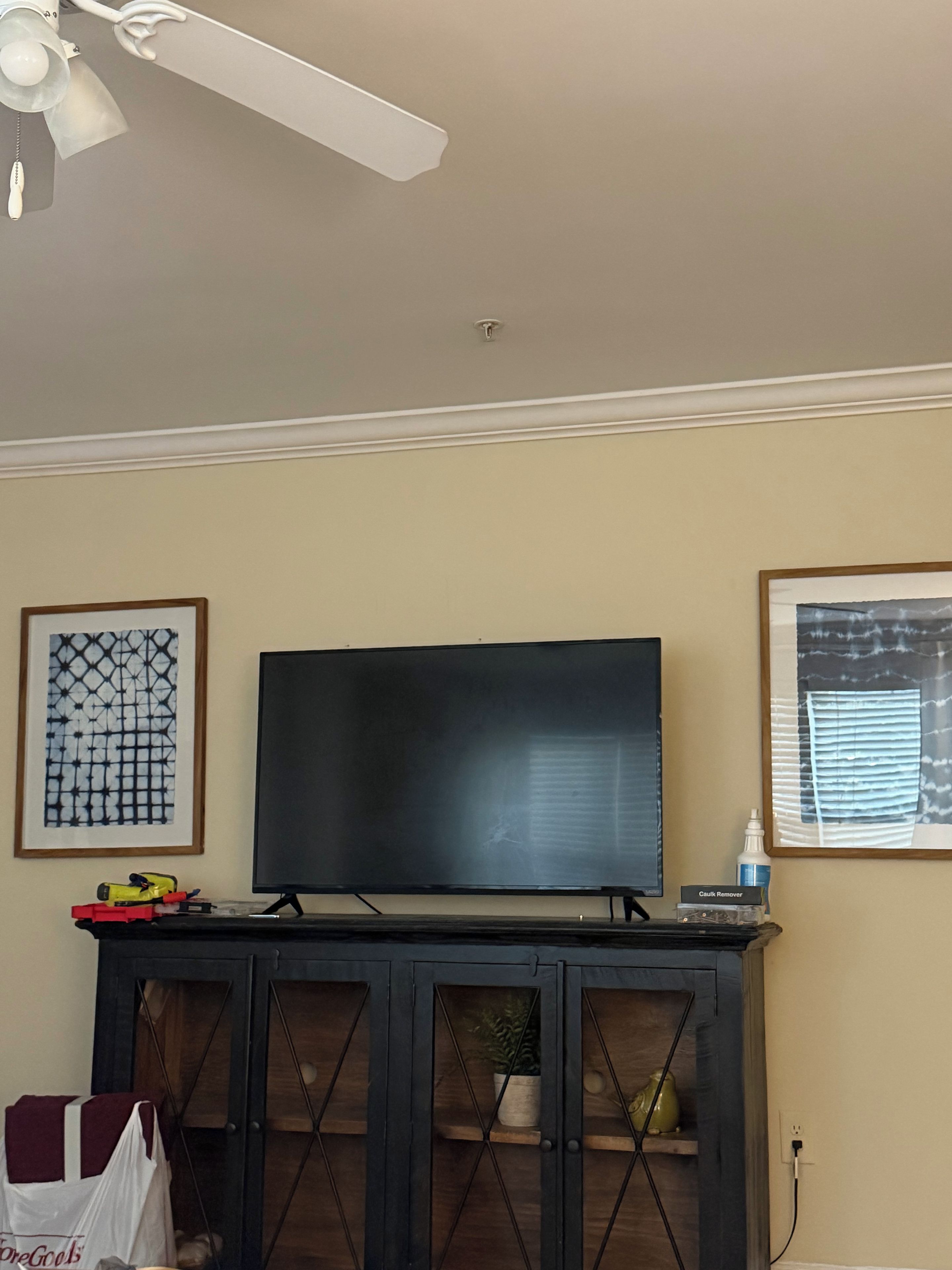 A living room with a flat-screen TV, a ceiling fan, and framed artwork on the walls.