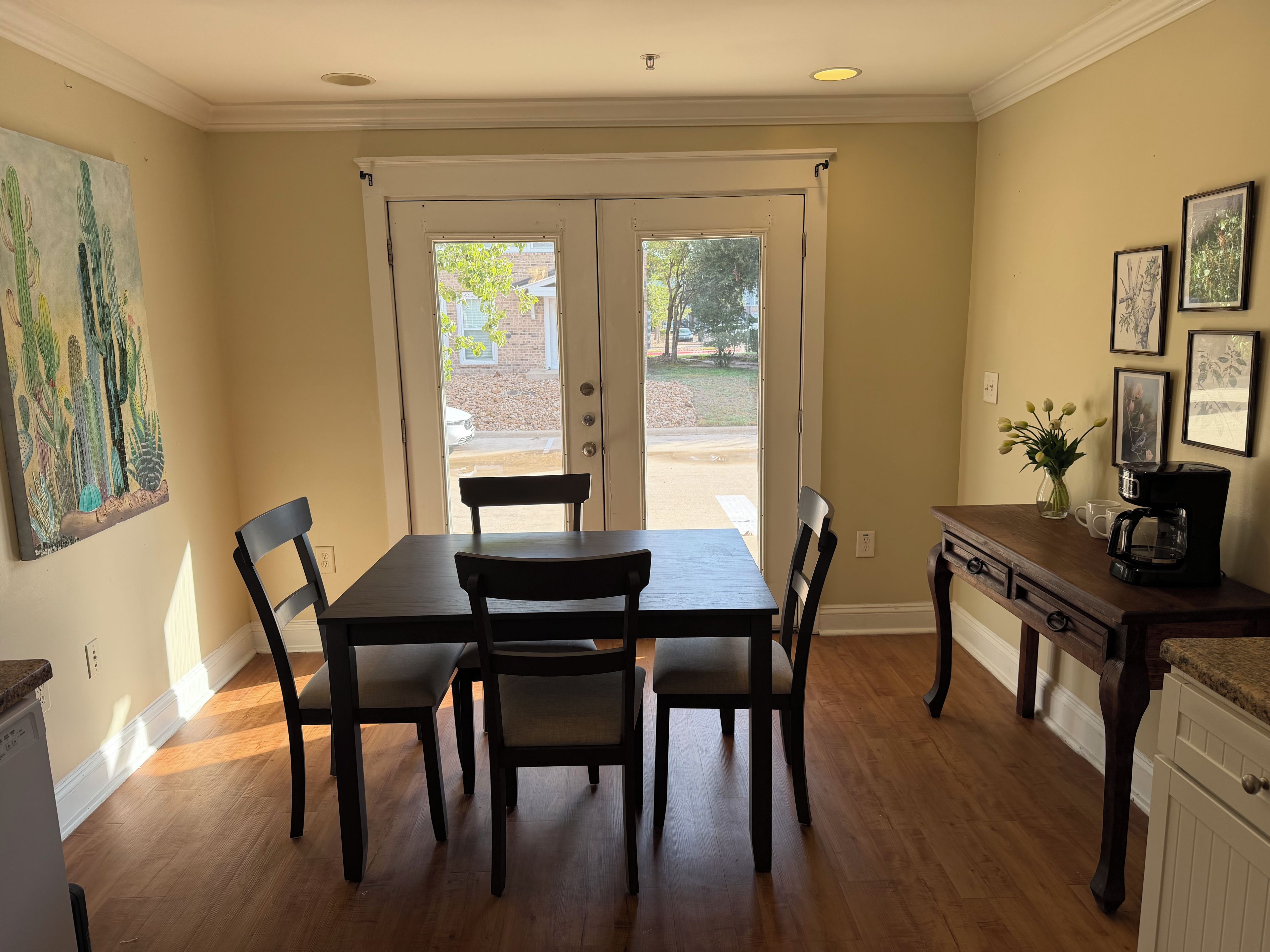 A dining area with a table and chairs, a coffee maker, and a painting on the wall.