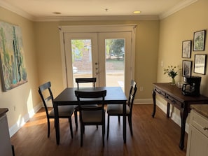 A dining area with a table and chairs, a coffee maker, and a painting on the wall.