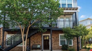 A two-story building with a brick facade, a balcony on the upper floor, and a staircase leading to the entrance.