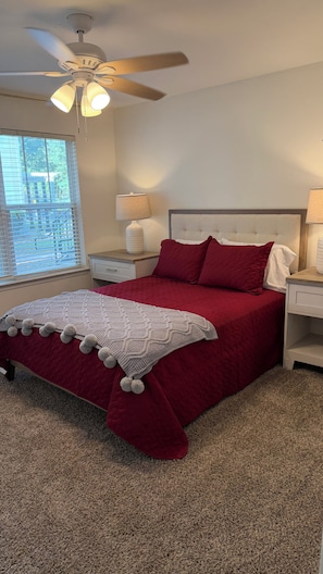 A bedroom with a bed, nightstands, a ceiling fan, and a window with blinds.