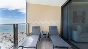 En balkong med två solstolar, ett litet bord och utsikt över stranden och havet.