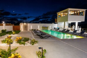 A modern outdoor pool area with lounge chairs and a bar area, surrounded by a landscaped garden. - Villa Camila is a stylish, modern one-bedroom apartment, centrally located. (Providenciales)