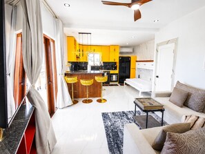 A modern living room with a sofa, a coffee table, and a dining area with yellow cabinets and a black countertop. - Villa Camila is a stylish, modern one-bedroom apartment, centrally located. (Providenciales)