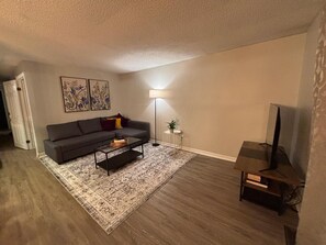 A living room with a sofa, coffee table, floor lamp, and a television. - 5 min to Clifton Hill and several attractions. Free parking & wifi (Niagara Falls)