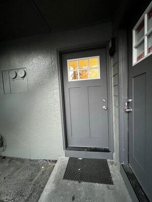 A gray door with a small window, a metal vent, and a concrete step leading to the door.