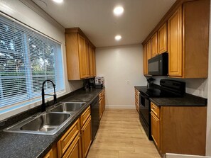 A modern kitchen with wooden cabinets, a stainless steel sink, a microwave, and a stove.
