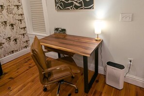 Un escritorio de madera con una silla, una lámpara de pared y un cesto de basura.