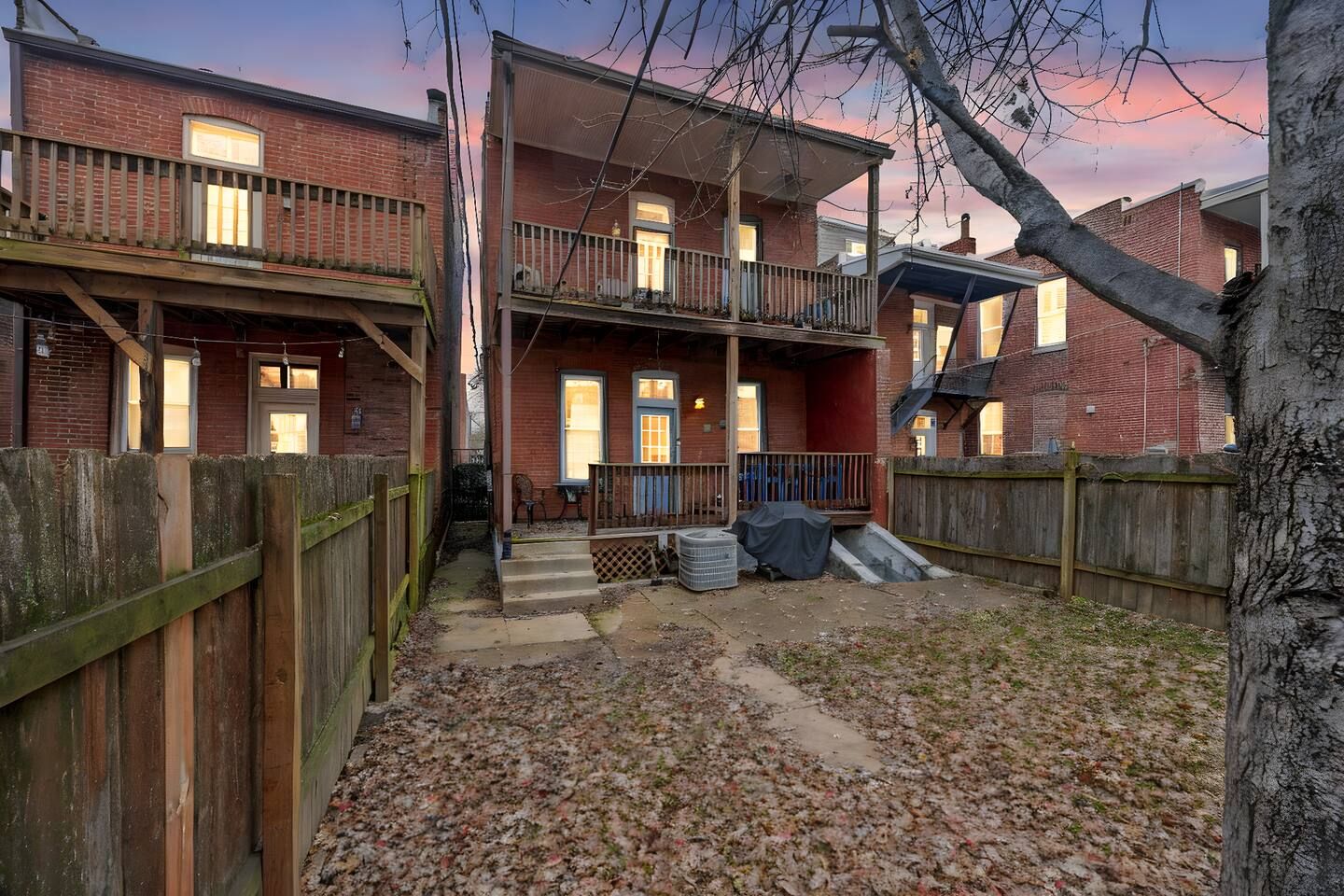 A two-story residential building with a balcony, a covered porch, and a fenced backyard.