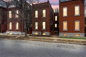 A row of red brick townhouses with multiple windows, a tree in the foreground, and a clear sky. - NEW! Benton Park Gem, Sleeps 8 & Dog Friendly - Stay Smiley Rentals (St. Louis)