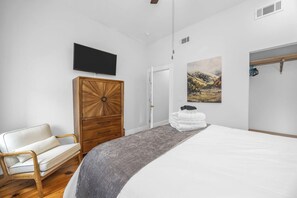 A bedroom with a bed, a wooden wardrobe, a chair, a painting on the wall, and a television mounted above the bed. - NEW! Benton Park Gem, Sleeps 8 & Dog Friendly - Stay Smiley Rentals (St. Louis)