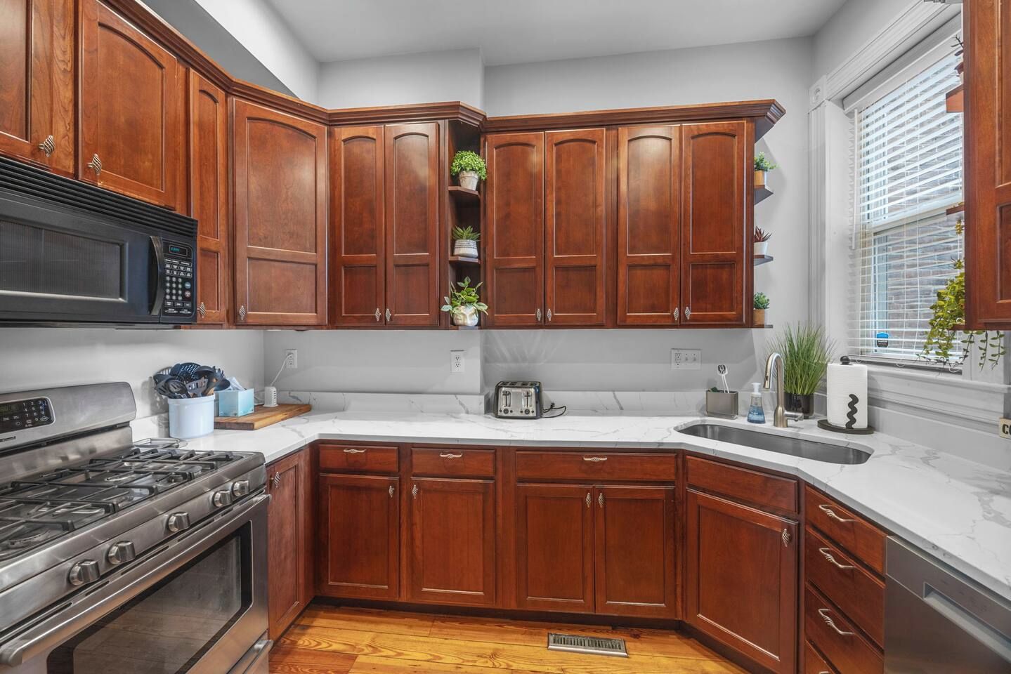 A kitchen with wooden cabinets, a stove, a microwave, and a sink.