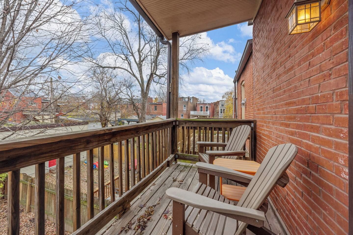 A wooden deck with a brick wall, two Adirondack chairs, and a table.